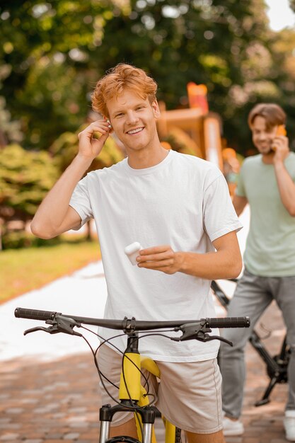 Sorridente attraente giovane zenzero che mette un auricolare wireless nel suo orecchio mentre il suo amico parla sullo smartphone