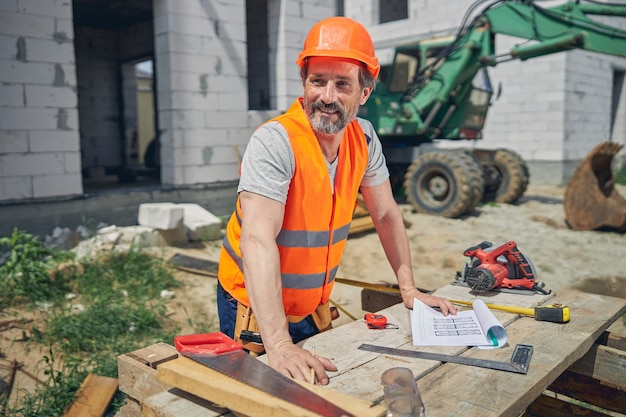 Sorridente attraente ingegnere civile appoggiando le mani su un tavolo di legno in un cantiere