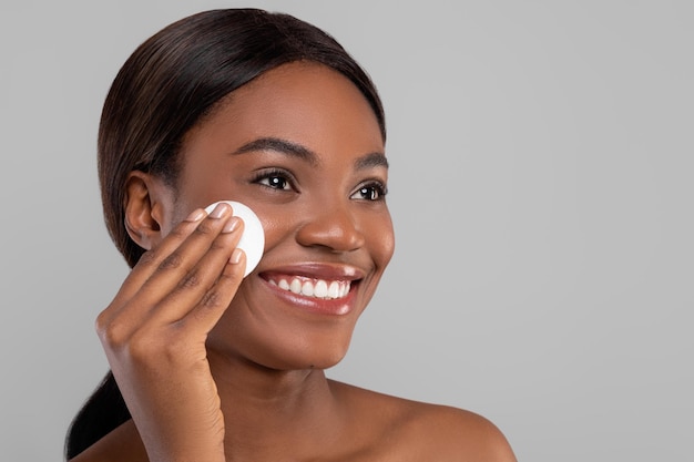 Sorridente attraente signora nera che pulisce il viso con il primo piano del tampone di cotone