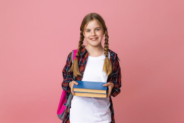 Sorridente bambina bionda 1012 anni in uniforme scolastica con zaino in possesso di libri isolati su sfondo rosa pastello ritratto in studio Il concetto di stile di vita dei bambini Istruzione a scuola