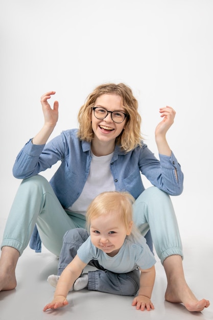 Sorridente bambina bionda dagli occhi azzurri che si appoggia sulle mani vicino alla giovane bella donna divertente madre