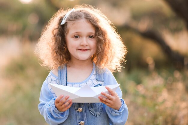 Sorridente bambina di 34 anni che tiene la barca di carta origami all'aperto