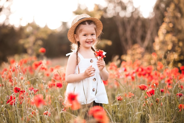 Sorridente bambina felice che tiene in mano un portafiori in un prato di papaveri