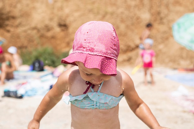 Sorridente bambina in costume da bagno, con un cappello panama sulla spiaggia.