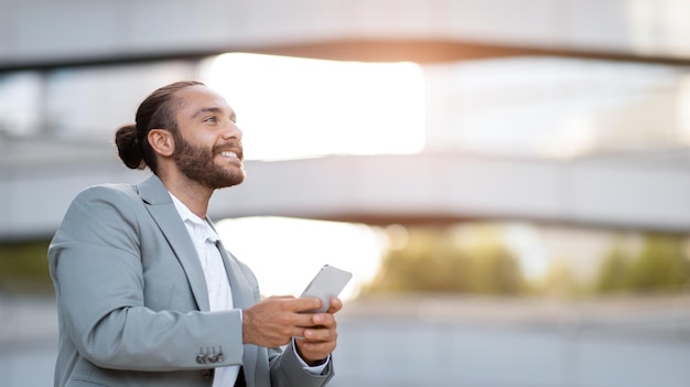 Sorridente bel giovane uomo d'affari con lo smartphone in mano in piedi all'aperto