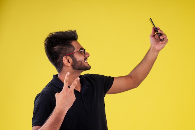 Sorridente bell'uomo indiano che fotografa selfie in studio su sfondo giallo.