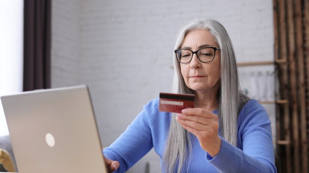 Sorridente bella anziana dai capelli grigi donna shopping online tenendo la carta di credito.