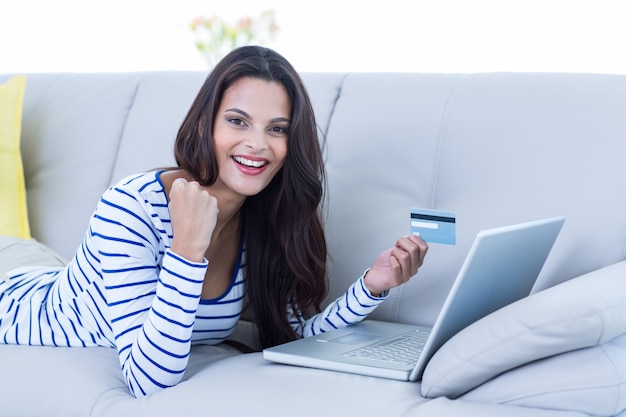 Sorridente bella bruna facendo shopping online sul divano