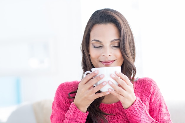 Sorridente bella bruna rilassante sul divano e tenendo la tazza