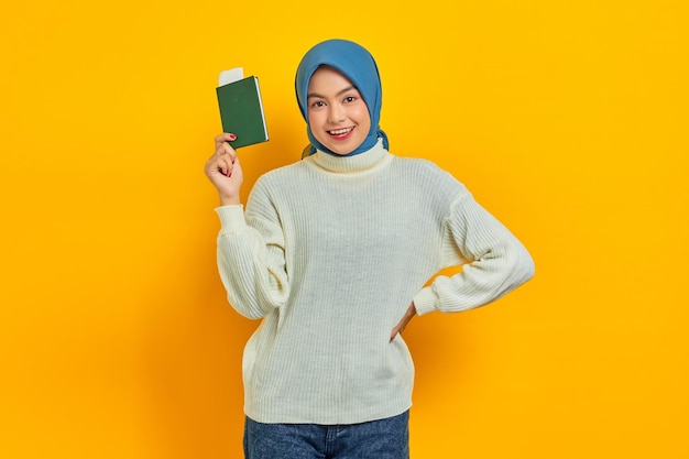 Sorridente bella donna asiatica in maglione bianco che mostra il passaporto isolato su sfondo giallo Summer Trip