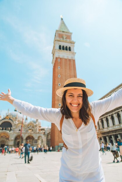 Sorridente bella donna caucasica alzare le mani al campanile di piazza della città di venezia sullo sfondo