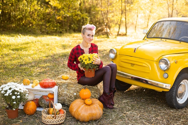 Sorridente bella donna con fiori e zucche in autunno parco sfondo vicino auto gialla