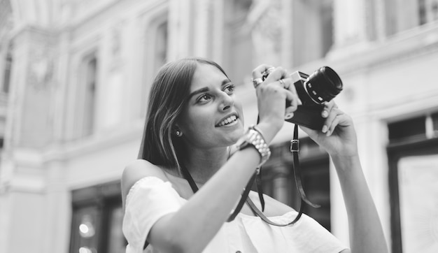 Sorridente bella donna con la retro macchina fotografica nelle sue mani mentre si scattano foto alla vecchia architettura urbana. Scopri nuovi posti. Bianco e nero