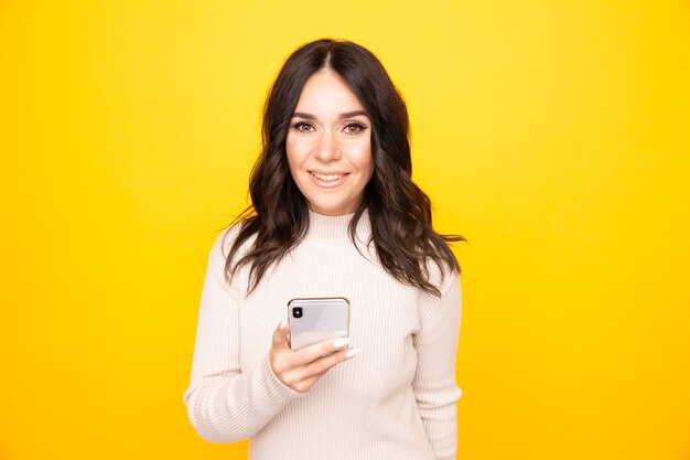 Sorridente bella donna con telefono in piedi isolato su sfondo giallo.