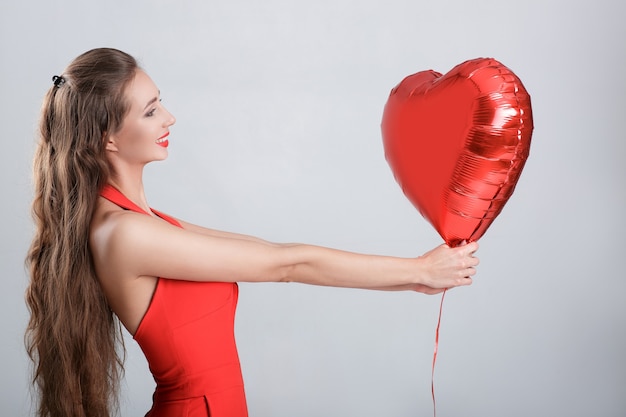 Sorridente bella donna riccia con palloncini d'aria a forma di cuore per il giorno di San Valentino