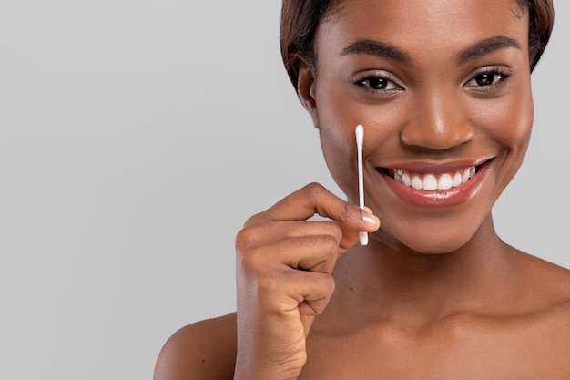 Sorridente bella giovane donna afroamericana con pelle perfetta mostra un batuffolo di cotone isolato su grigio