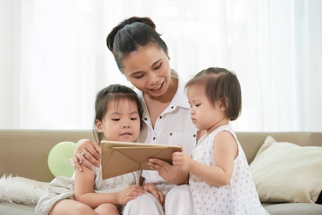 Sorridente bella giovane donna che mostra cartone animato educativo ai suoi due bambini piccoli