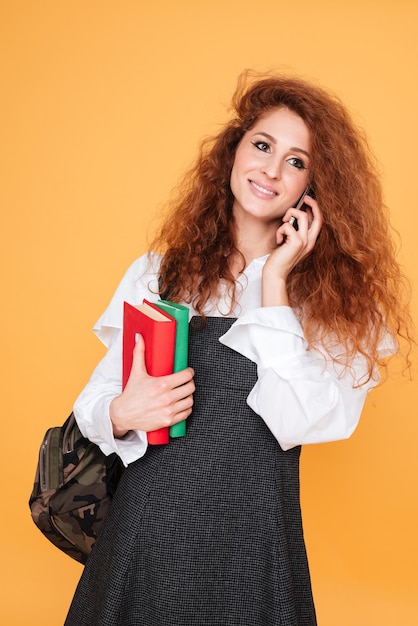 Sorridente bella giovane donna con libri e zaino parlando al cellulare