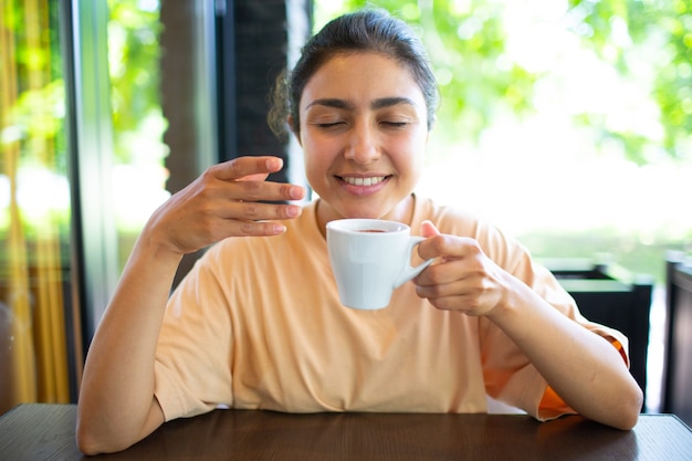 Sorridente bella giovane donna indiana che beve caffè al bar esterno outside