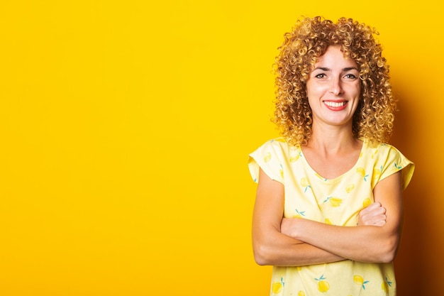 Sorridente bella giovane donna riccia con le braccia incrociate su uno sfondo giallo