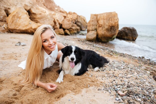 Sorridente bella giovane donna sdraiata con il cane sulla spiaggia