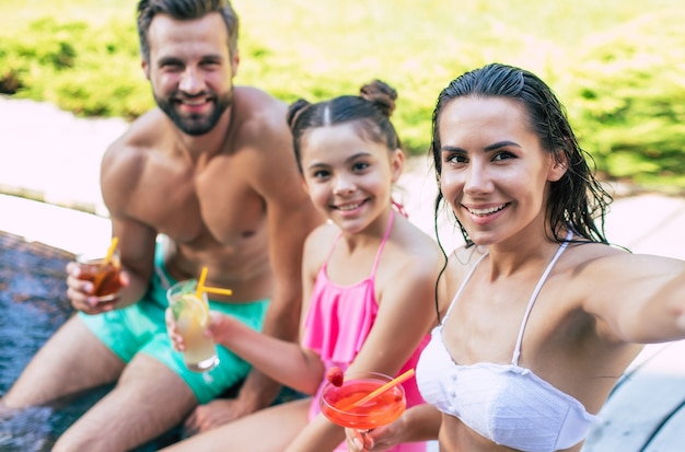 Sorridente bella giovane famiglia felice facendo selfie su smart phone mentre riposano nella piscina dell'hotel e si divertono.