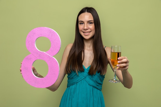 Sorridente bella ragazza il giorno della donna felice tenendo il numero otto con un bicchiere di champagne