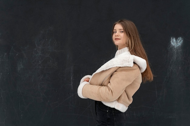 Sorridente bella ragazza in breve cappotto di pelle di pecora beige Giovane donna in capispalla elegante su sfondo nero Spazio per il testo