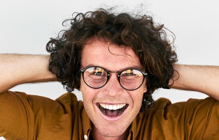 Sorridente bello felice giovane uomo d'affari con gli occhiali Studente maschio in posa su sfondo bianco muro Ragazzo intelligente in camicia e occhiali con capelli ricci che guarda alla telecamera Emozioni della gente