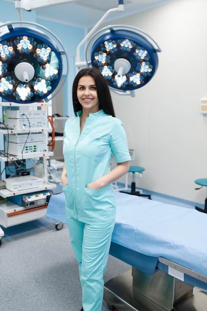 Sorridente chirurgo femminile pone al tavolo operatorio, lampada sullo sfondo