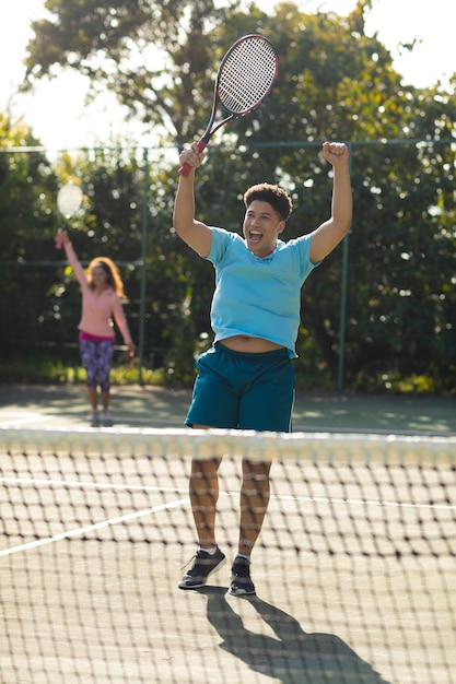 Sorridente coppia biraziale che gioca a tennis tifo sul soleggiato campo da tennis all'aperto. Inclusività, sport, hobby sani, competizione, fitness e concetto di tempo libero.