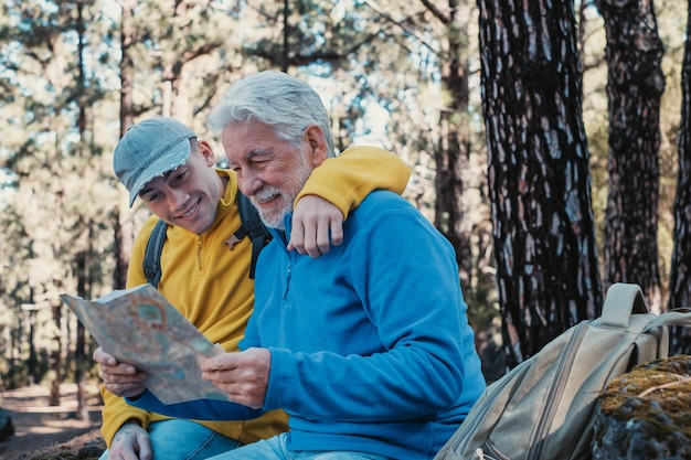 Sorridente coppia caucasica di nonno anziano e giovane nipote che fanno escursioni insieme nei boschi riposando guardando la mappa Vecchia e nuova generazione che condividono la passione per la natura e lo stile di vita sano