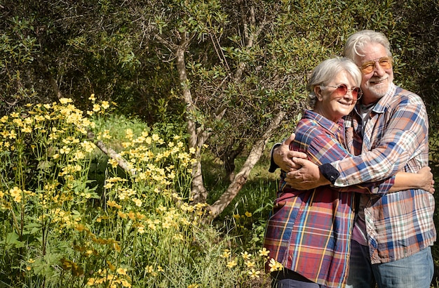 Sorridente coppia di anziani nella foresta che si abbracciano godendosi la primavera e la fioritura. Due pensionati che amano uno stile di vita sano