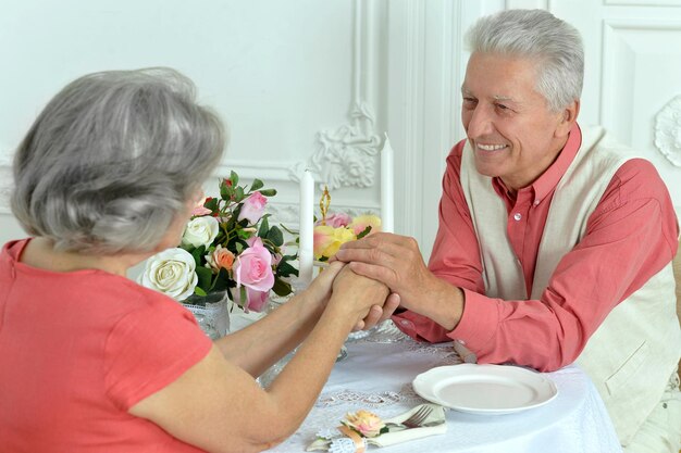 Sorridente coppia di anziani seduti al tavolo da pranzo e tenendosi per mano insieme