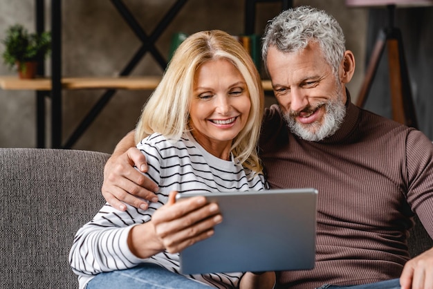 Sorridente coppia di mezza età con tavoletta digitale sul divano di casa
