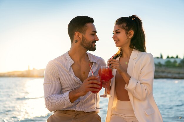 Sorridente coppia etnica che beve cocktail sull'argine