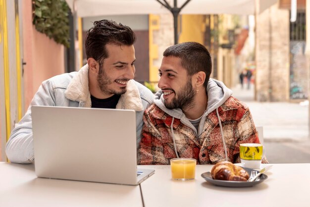 Sorridente coppia gay al caffè utilizzando il computer portatile