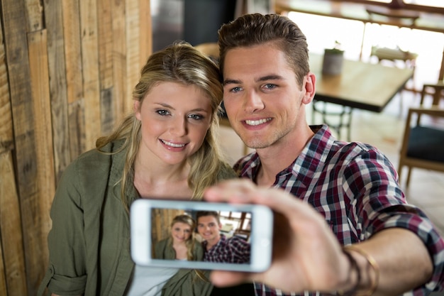 Sorridente coppia giovane tenendo selfie con il telefono cellulare nella caffetteria