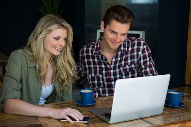 Sorridente coppia giovane utilizzando laptop a tavola nella caffetteria