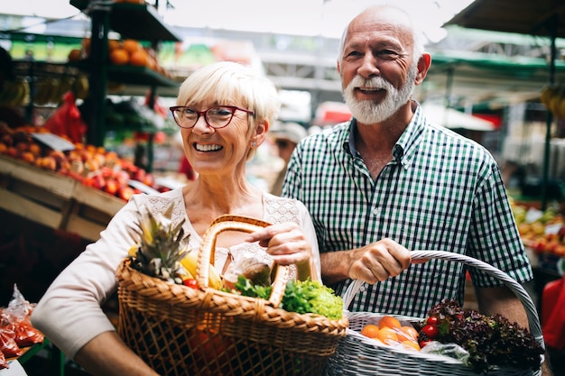 Sorridente coppia senior che tiene cesto con verdure al negozio di alimentari