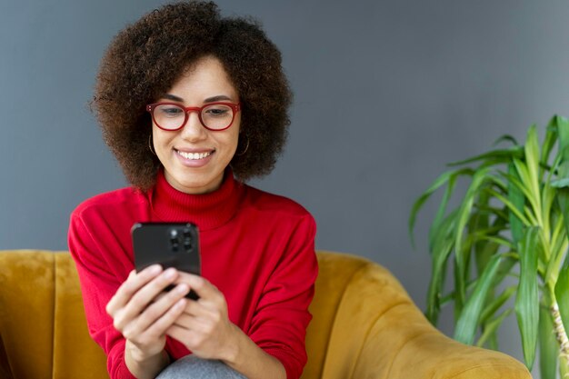 Sorridente donna afroamericana che tiene il cellulare guardando video seduti a casa