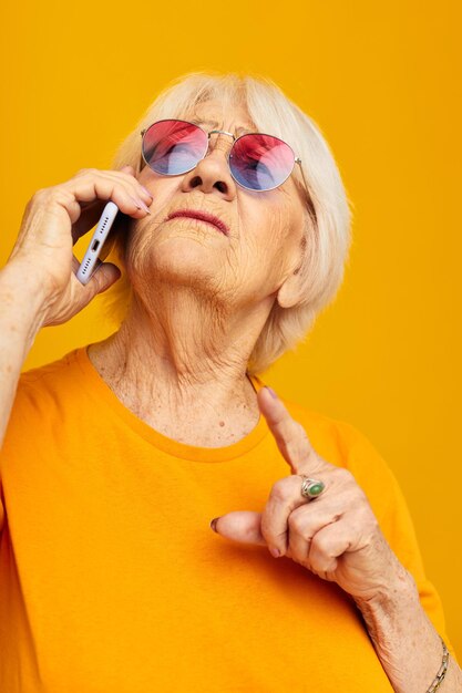 sorridente donna anziana felice stile di vita in magliette gialle con emozioni del primo piano del telefono. Foto di alta qualità