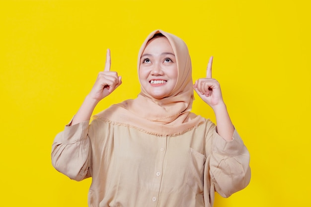 Sorridente donna asiatica che indossa l'hijab con il dito puntato isolato su sfondo giallo chiaro banner