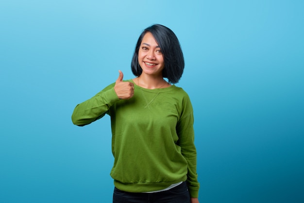 Sorridente donna asiatica che mostra i pollici su sfondo blu