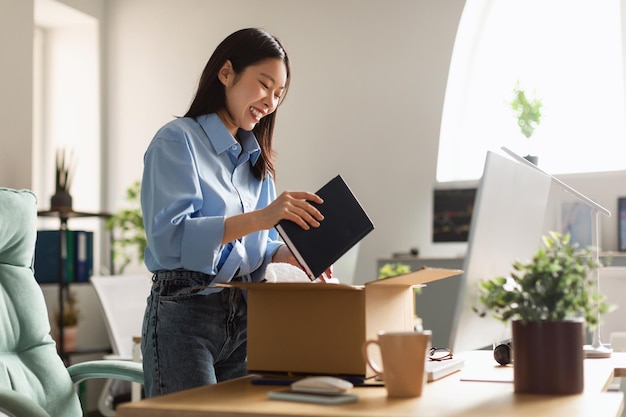 Sorridente donna asiatica disimballaggio scatola al nuovo posto di lavoro