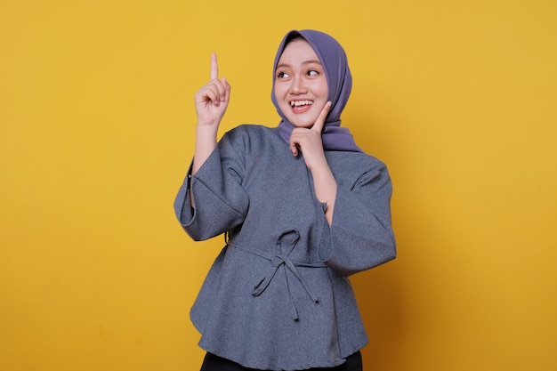 Sorridente donna asiatica felice che indossa l'hijab con il dito puntato isolato su sfondo giallo chiaro banner