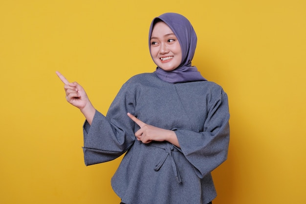 Sorridente donna asiatica felice che indossa l'hijab con il dito puntato isolato su sfondo giallo chiaro banner
