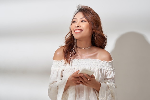 Sorridente donna asiatica positiva con bel viso emotivo che ascolta musica su bianco