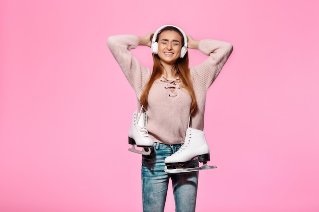 Sorridente donna attraente che tiene i pattini da ghiaccio e ascolta musica con le cuffie