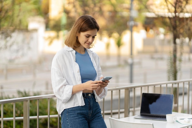 Sorridente donna attraente che utilizza il telefono cellulare che comunica chat online leggendo il messaggio di testo